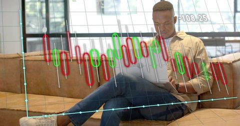 Young Man Analyzing Candlestick Stock Charts on Laptop in Modern Lounge Workspace