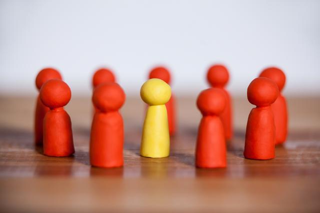 Conceptual image of yellow figurine standing between a group of red figurines