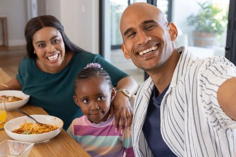 Diverse family taking selfie while sharing pasta meal at bright home dining table