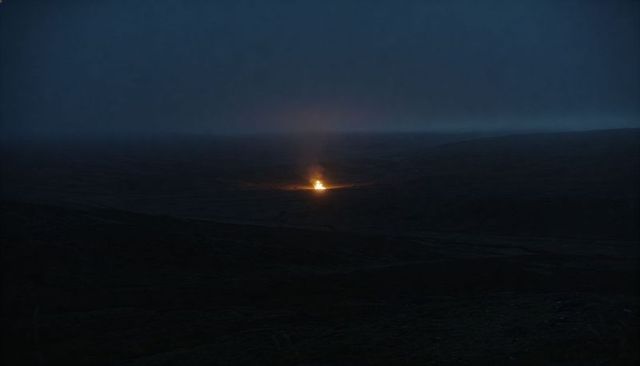 Solitary bonfire on remote moorland at night illuminating misty horizon and ember glow