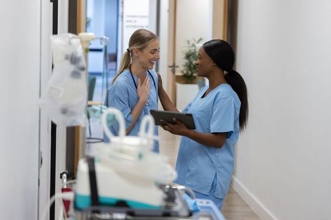 Diverse nurses collaborating in hospital corridor holding tablet and stethoscope