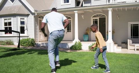 Father and son playing soccer on sunny front lawn of suburban home