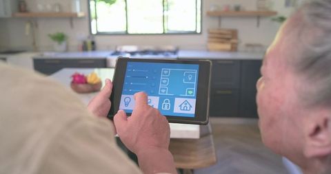Asian senior couple using tablet for smart home control in modern daylit kitchen