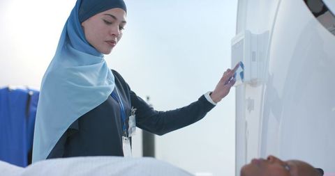 African american female radiology technologist wearing hijab operating ct gantry with patient