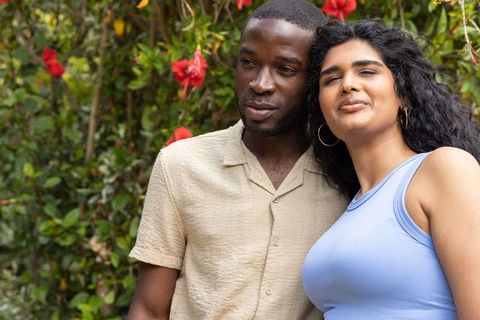 Diverse couple leaning together in lush garden with hibiscus, casual summer fashion