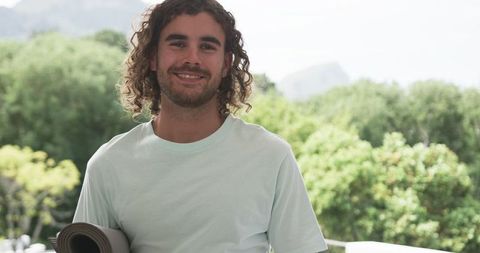 Young man holding yoga mat outdoors in tranquil natural setting