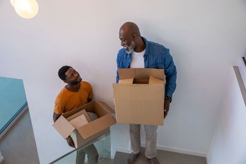 African American Father and Son Moving Boxes in Modern Home