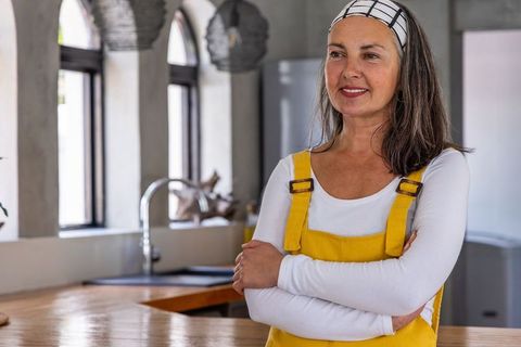 Middle-aged woman standing confidently in modern kitchen wearing yellow overalls
