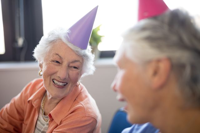 Smiling senior women wearing party hats talking at nursing home
