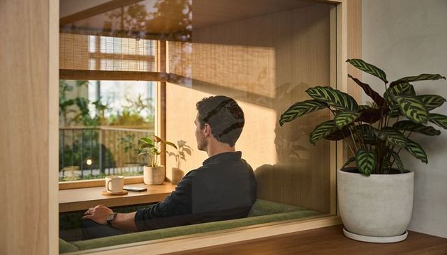 Man relaxing in cozy wooden window nook sipping coffee and viewing smartphone in sunlight