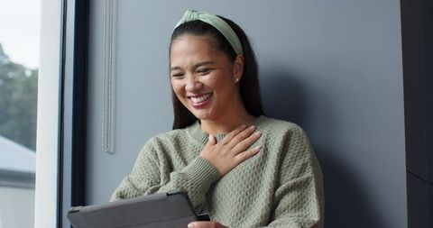 Asian woman relaxing with tablet indoors wearing mint green sweater