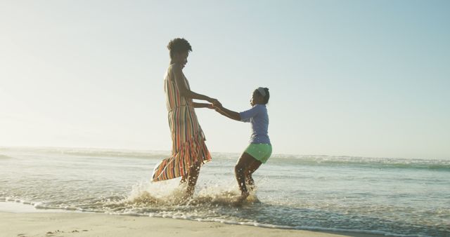 Mother and daughter holding hands while playing in shallow water on the beach during sunset. Ideal for travel brochures, family vacation advertisements, summer campaigns, or articles about family bonding and outdoor activities.