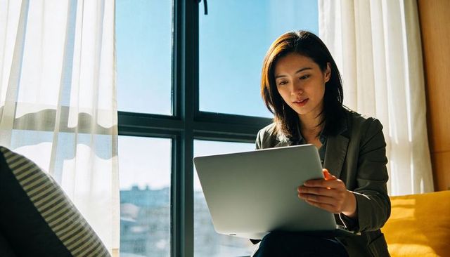 Business professional working on laptop by sunlit window in minimalist home office