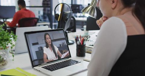 Woman Participating in Remote Video Meeting on Laptop at Open-Plan Office Desk