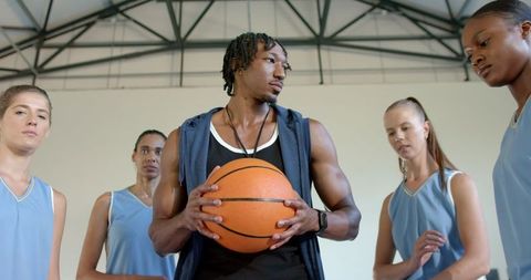 Basketball Team Huddling with Coach Holding Ball in Gym