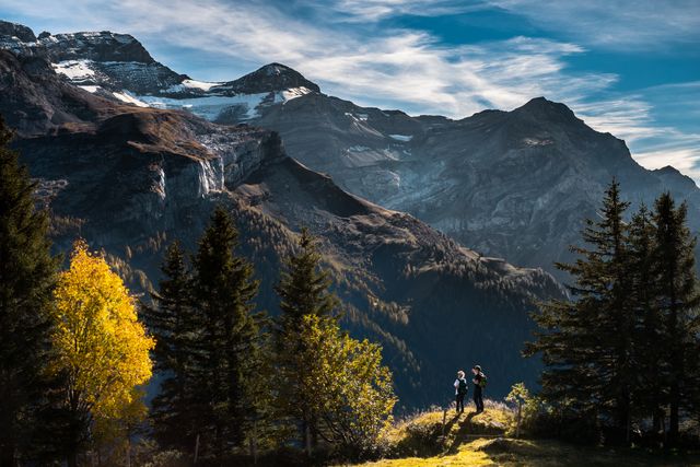 Couple hiking in vibrant autumn season, against dramatic mountain background with snow-capped peaks. Ideal for travel blogs, nature photography, outdoor adventure promotions, and environmental awareness campaigns.