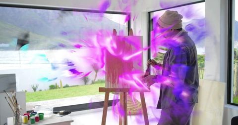 Artist painting at sunlit coastal studio with purple-pink mist, easel and paints