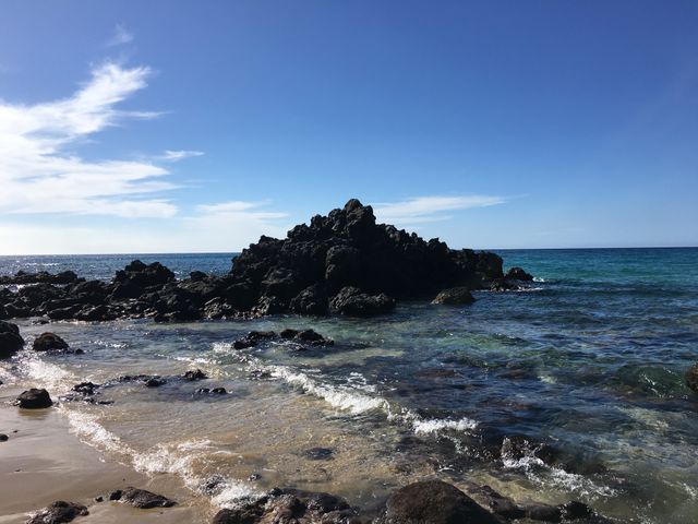 Rocky beachfront with clear blue waters and a clear sky creates a serene, natural landscape ideal for backgrounds, travel brochures, and relaxation-themed promotions.