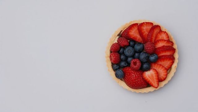 Displaying mixed berry tart on white tabletop with fluted crust overhead and copy space