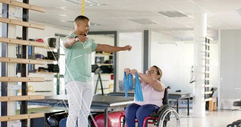 Therapist Guiding Wheelchair User Pulling Resistance Band During Rehabilitation Session