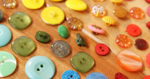 A variety of colorful buttons are spread out on a wooden surface, showcasing an array of sizes and designs. These buttons could be used for crafts, sewing projects, or as decorative elements.