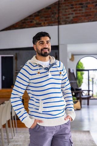 Confident man standing in modern rustic kitchen wearing striped sweater and cargo pants