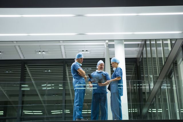 Team of surgeons in blue scrubs discussing an x-ray in a modern hospital corridor. Ideal for use in healthcare, medical teamwork, hospital operations, and professional consultation contexts.