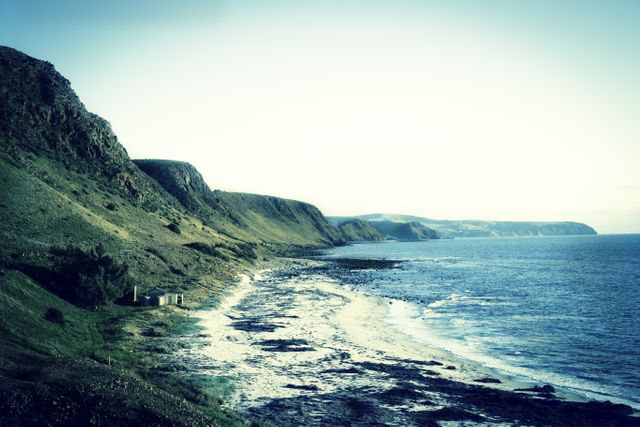 This serene image of a cliffside coast with gentle waves hitting the shoreline under the setting sun creates a peaceful atmosphere. It is suitable for travel blogs, nature websites, and relaxation-themed content. The tranquil scenery is perfect for use in promoting coastal destinations or experiencing the outdoors.