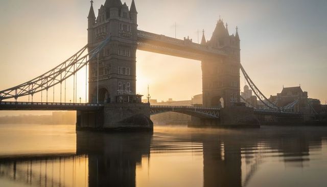 Tower bridge glowing in golden sunrise over river thames with calm reflections