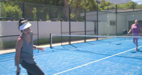 Women playing paddle tennis on vibrant blue outdoor court under bright sunny sky