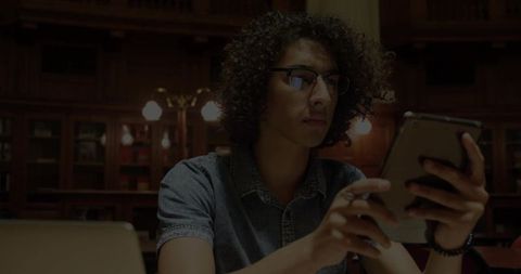 Curly haired man engaged with tablet in classic library ambience