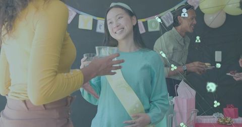 Smiling woman wearing sash raising glass at pastel baby shower with friends
