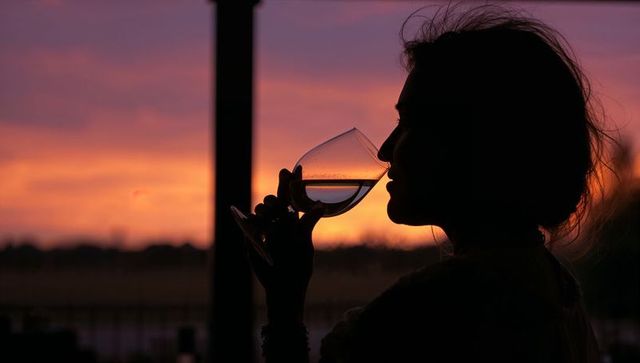 Woman silhouette sipping wine on balcony at vibrant orange and purple sunset