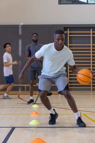 Male athlete dribbling through cone agility drill on indoor basketball court