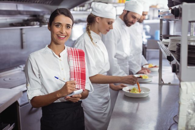 Portrait of waitress standing with notepad in commercial kitchen