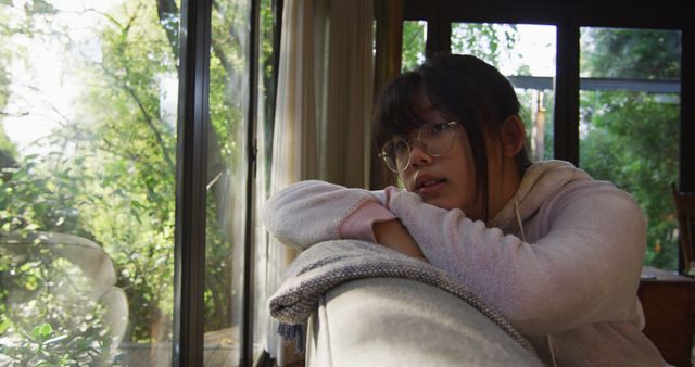 Asian girl looking through window and lying on couch. at home in isolation during quarantine lockdown.