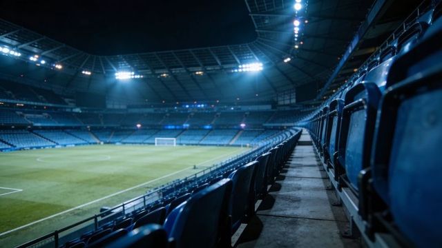 Wide empty blue stadium seats at night under floodlights with soccer pitch and aisle view