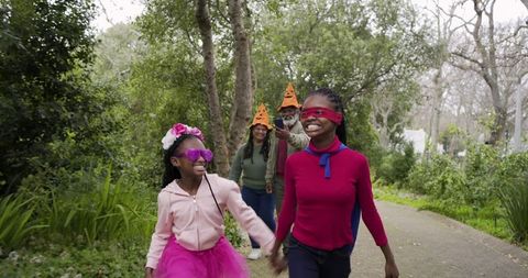 Black family enjoying playful halloween park walk with kids in capes, tutus and blindfolds