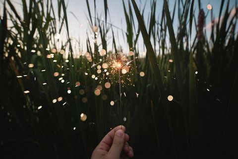 Hand Holding Sparkler in Grassy Field at Twilight