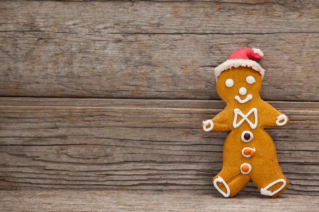 Gingerbread man wearing a Santa hat leaning against a rustic wooden background. Perfect for holiday-themed designs, Christmas cards, festive advertisements, and seasonal blog posts.