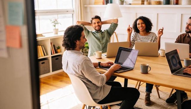 Startup team collaborating around wooden table with laptops and coffee in bright office