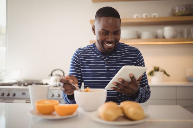 Smiling man using a digital tablet while having breakfast in kitchen at home