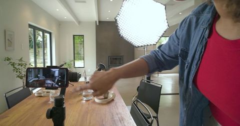 Woman filming product demo with smartphone gimbal and softbox lighting in modern interior
