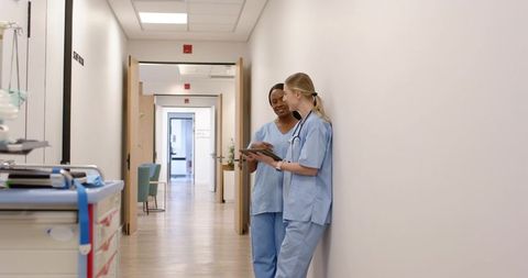 Two nurses consulting on tablet in hospital corridor, teamwork and clinical communication