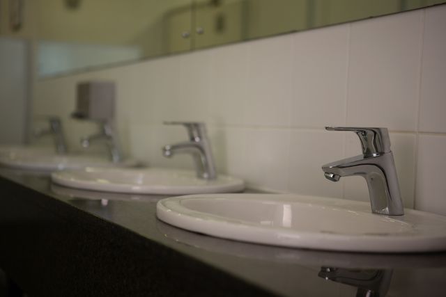 Clean bathroom sinks with modern faucets in a school setting. Ideal for illustrating hygiene, school facilities, public restrooms, or educational environments. Useful for articles on school infrastructure, cleanliness, or plumbing services.