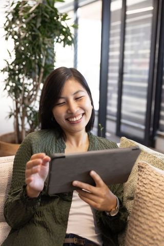 Smiling woman relaxing on sofa using digital tablet at home