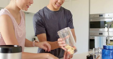 Young couple preparing banana-strawberry smoothie at kitchen island healthy lifestyle