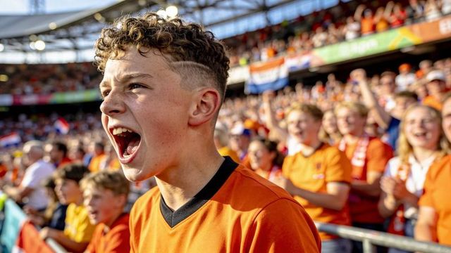 Curly-haired teen shouting and cheering in orange crowd at stadium football match
