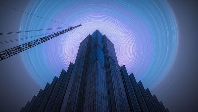Brutalist skyscraper reaching into swirling star trail vortex with construction crane