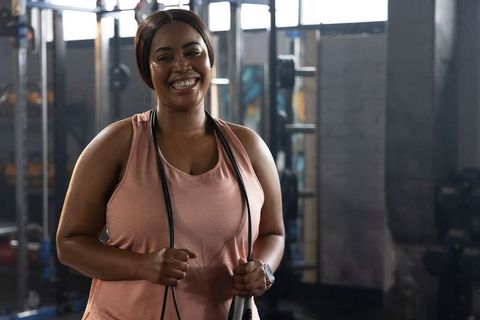 African american woman smiling while holding jump rope in gym wearing fitness tracker